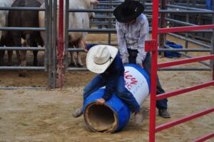 A young boy learns rodeo skills with guidance at a ranch setting.